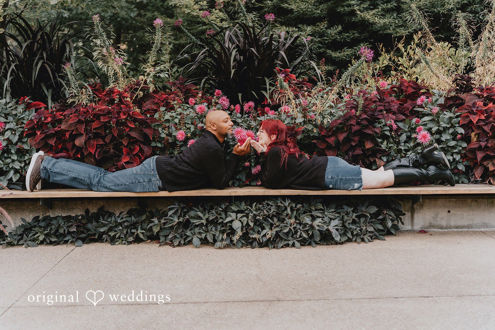 Nikki + Kevin Nikki and Kevin lying on a stone ledge by red flowers at Denver Botanic Gardens