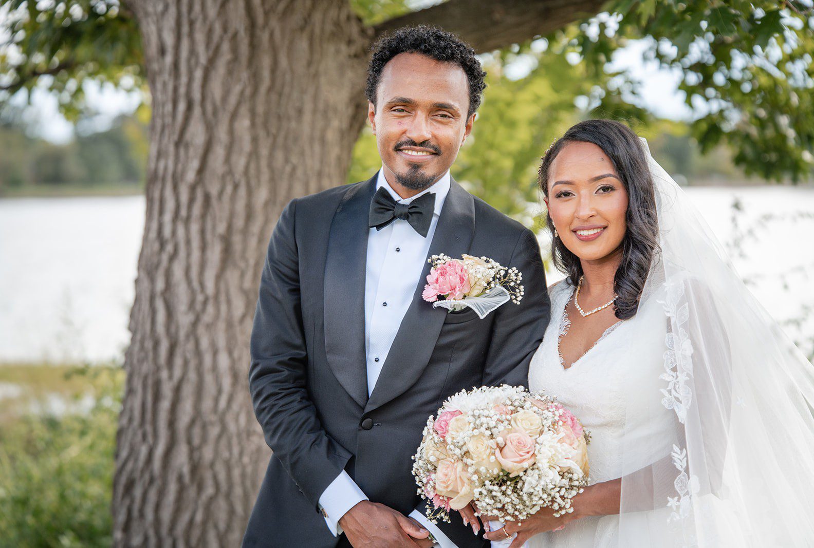 Bride and groom smiling beneath a tree, captured by Denver wedding photographers from Original Weddings at Nuur Event Center