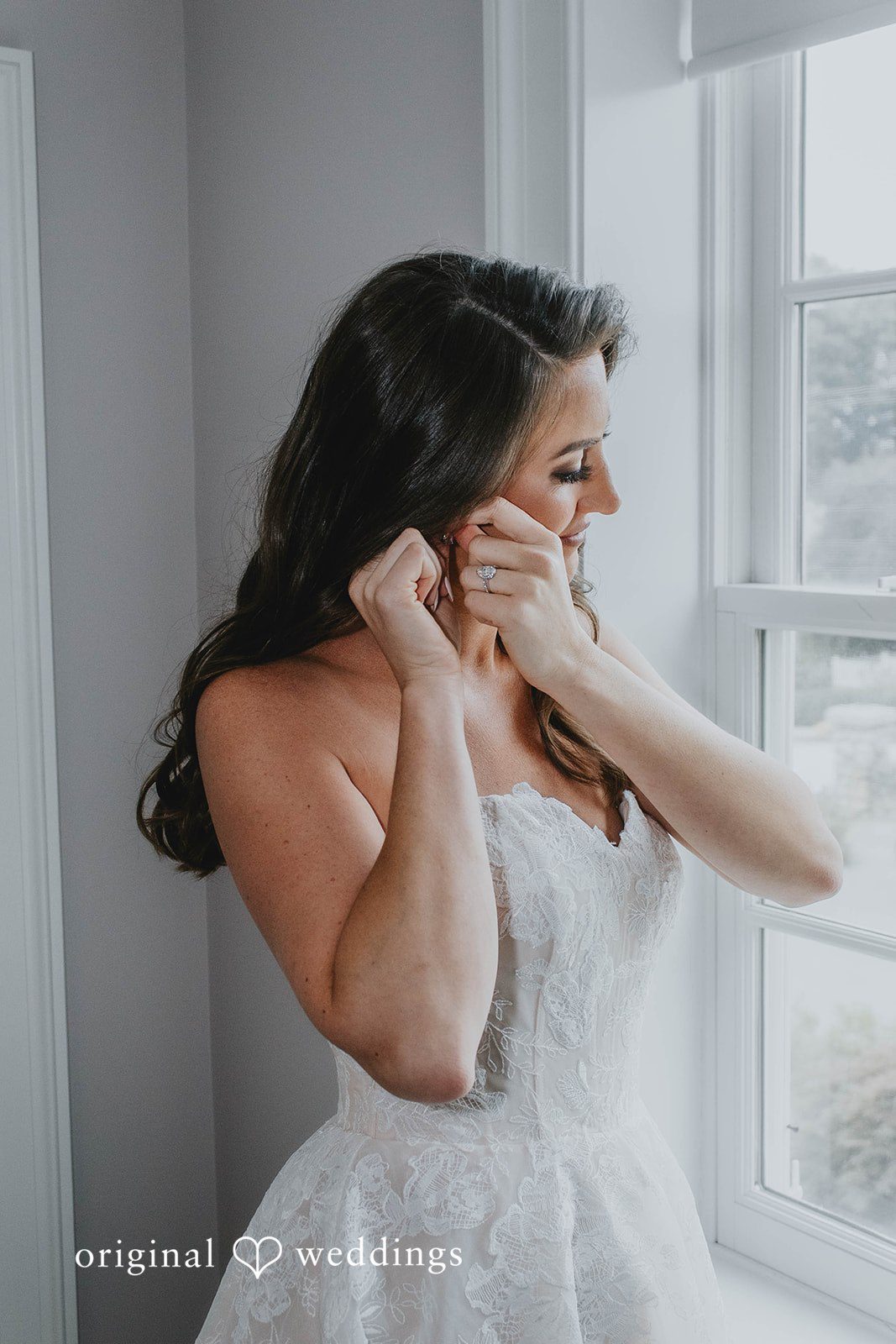 Alexa + Frank Bride putting on her earrings by the window