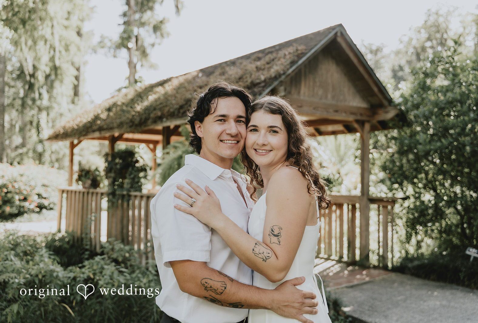 Larissa and Harley smiling in front of a wooden gazebo, captured by Engagement Photography Services from Original Weddings at Eureka Springs Conservation Park