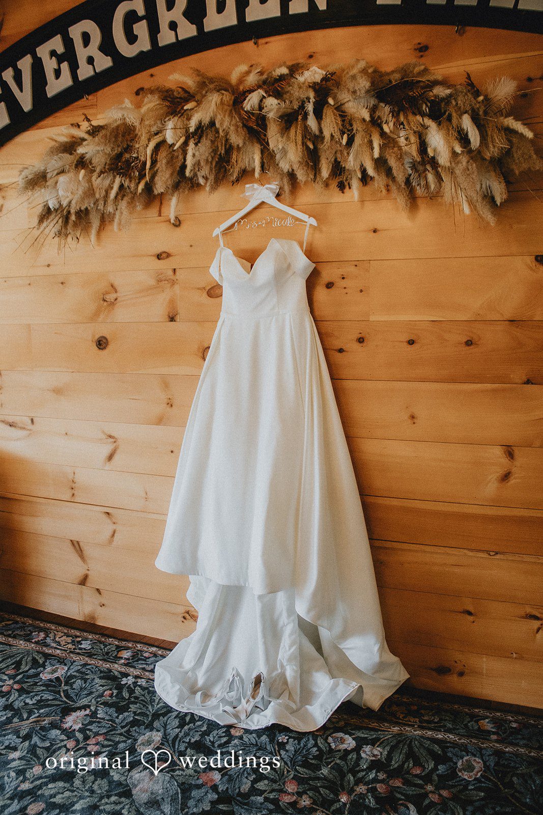 Sarah + Christopher A white wedding dress hanging on a wooden wall.