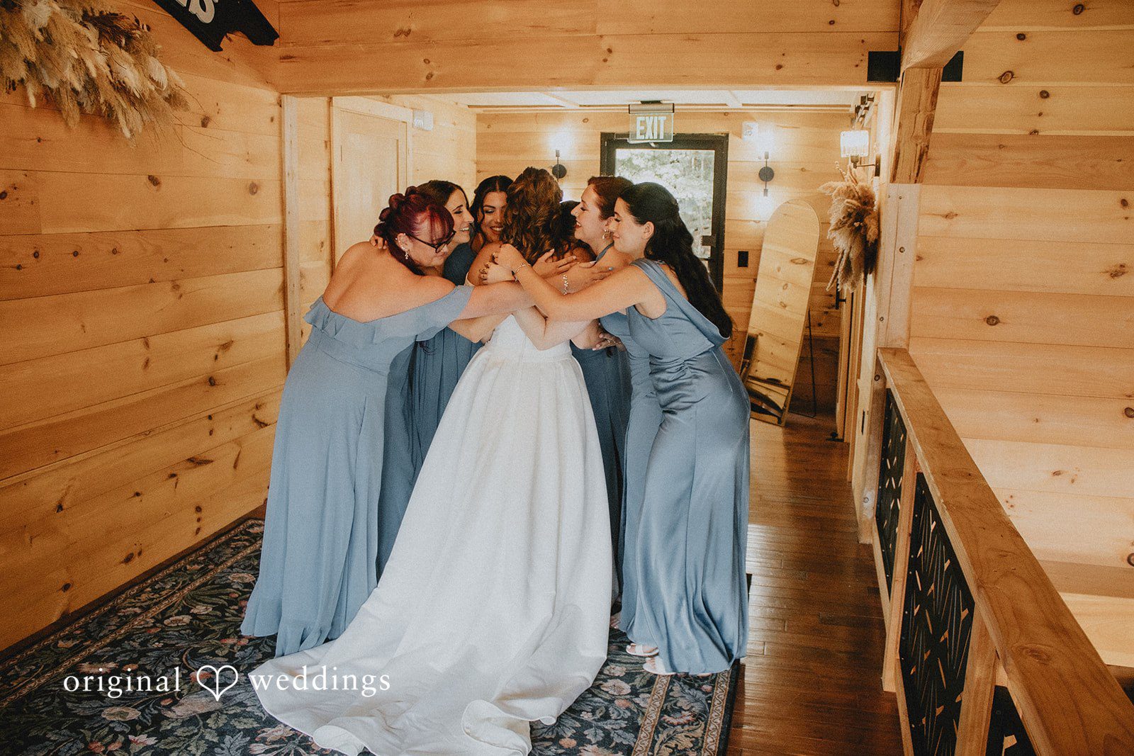 Sarah + Christopher A bride in a white gown standing in a wooden hallway alongside bridesmaids in blue.