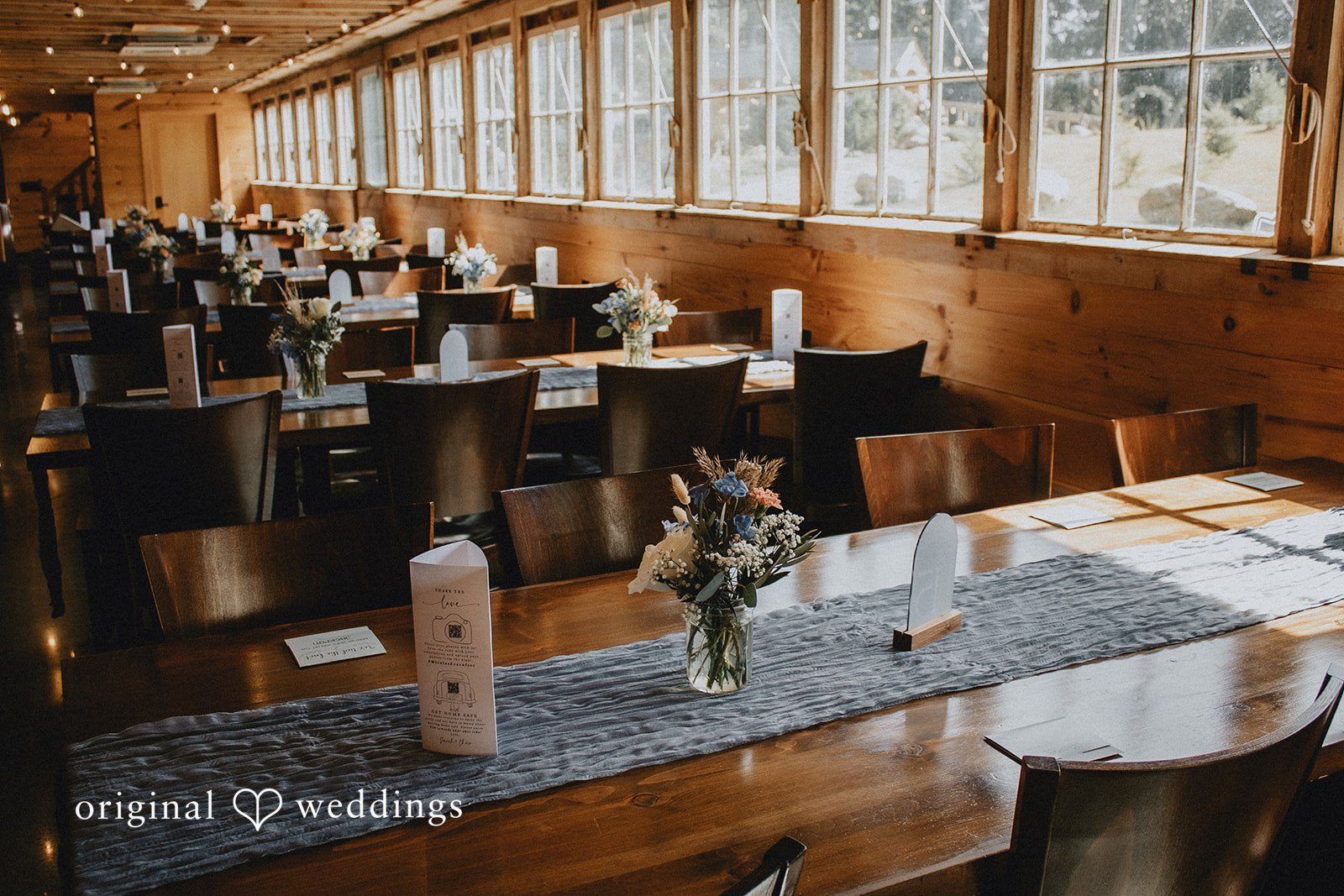 Sarah + Christopher A close-up view of an empty reception table setting with plates and glasses inside a log structure.