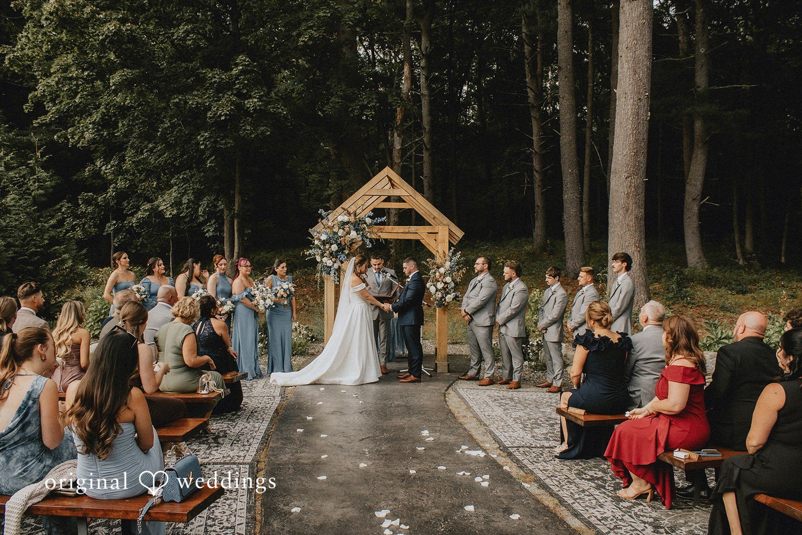 Sarah + Christopher Guests seated in rows watching an ongoing ceremony in a wooded clearing.