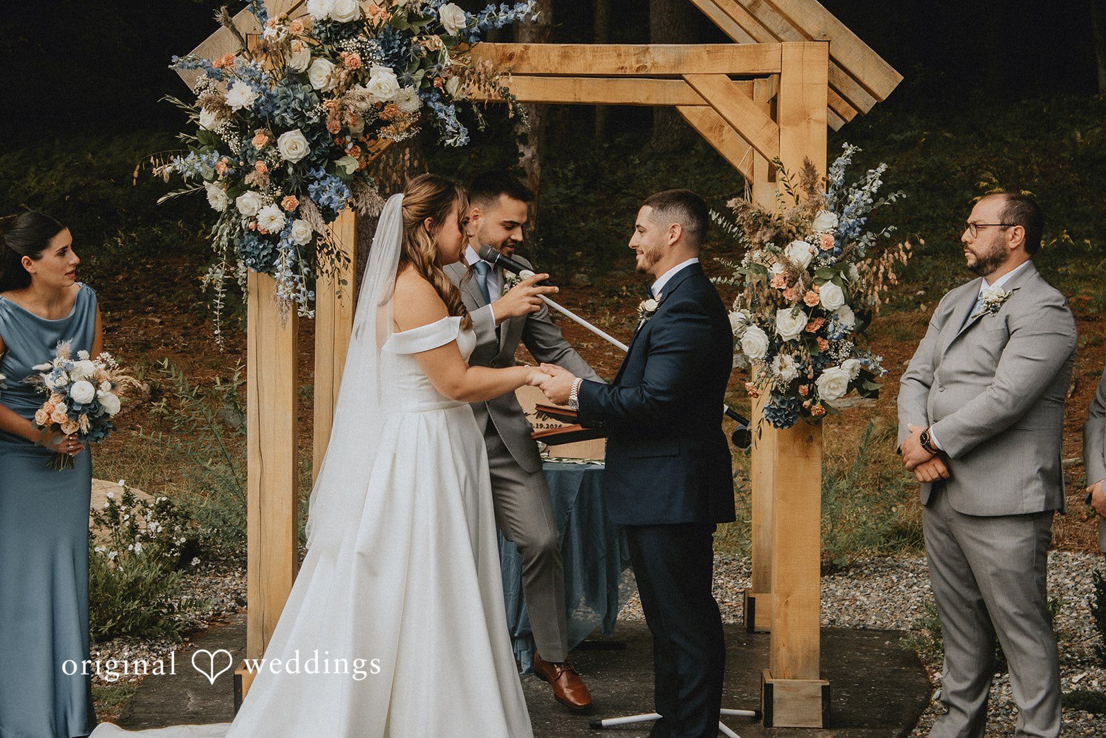 Sarah + Christopher A bride and groom holding hands during the wedding ceremony under a wooden arbor.
