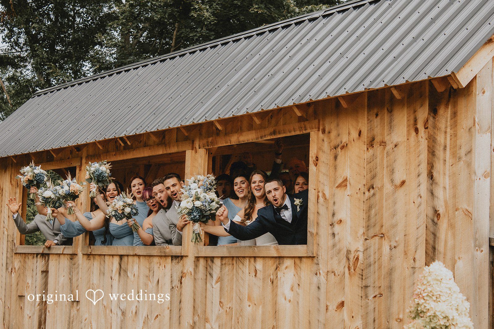 Sarah + Christopher A wedding party gathered along the window opening of a rustic wooden building.