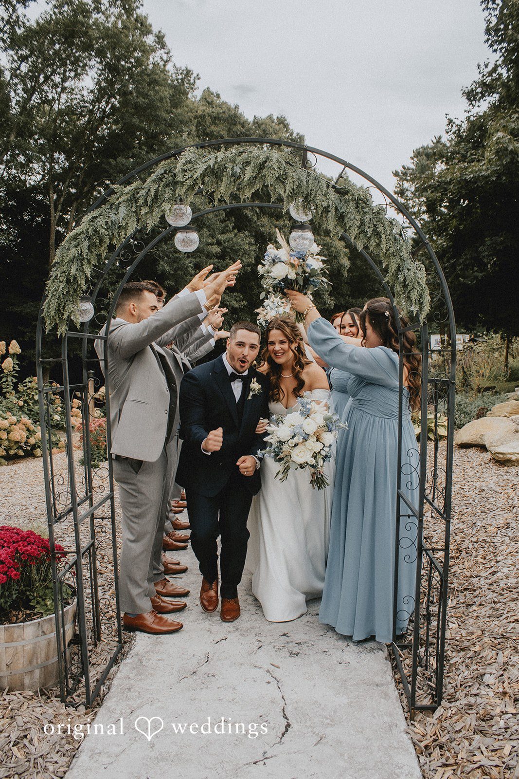 Sarah + Christopher Members of a wedding party standing together under a floral-decorated archway.