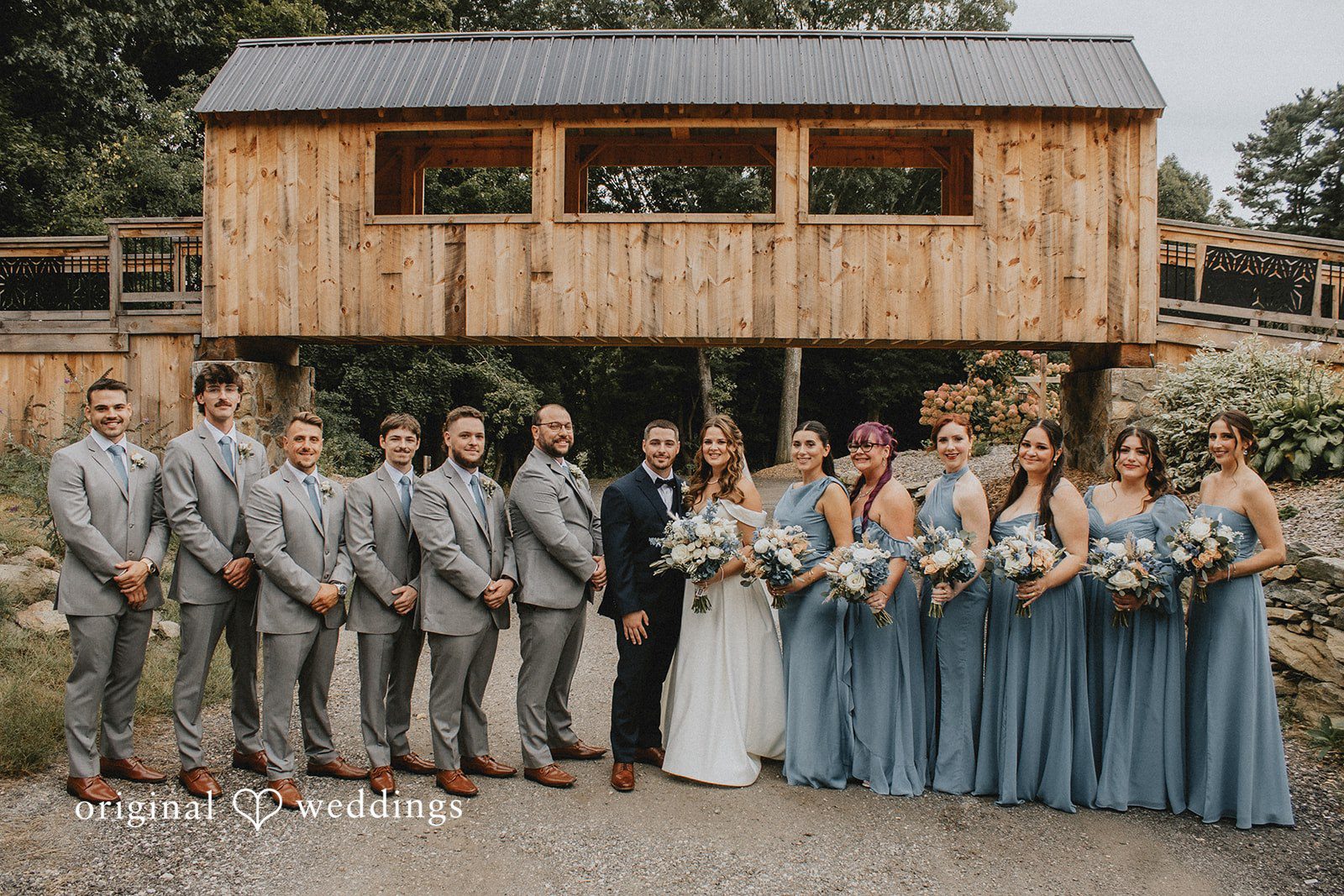 Sarah + Christopher A wedding party in formal wear lined up in front of a wooden structure.