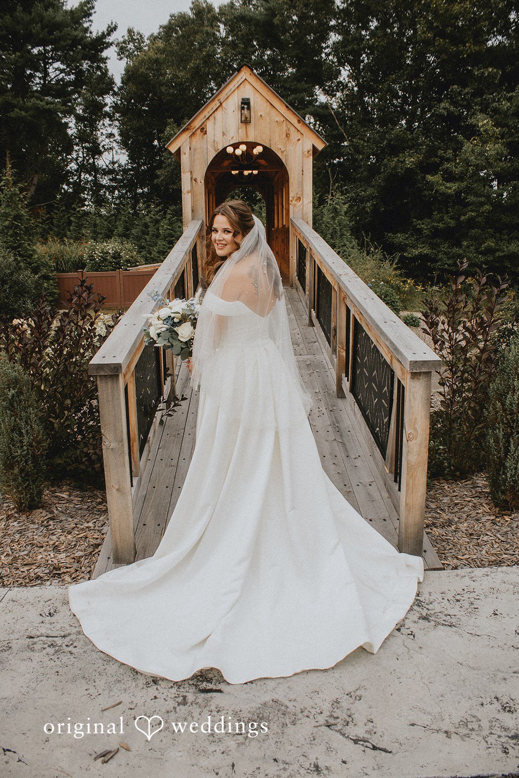 Sarah + Christopher A bride in a white gown walking across a small wooden bridge.