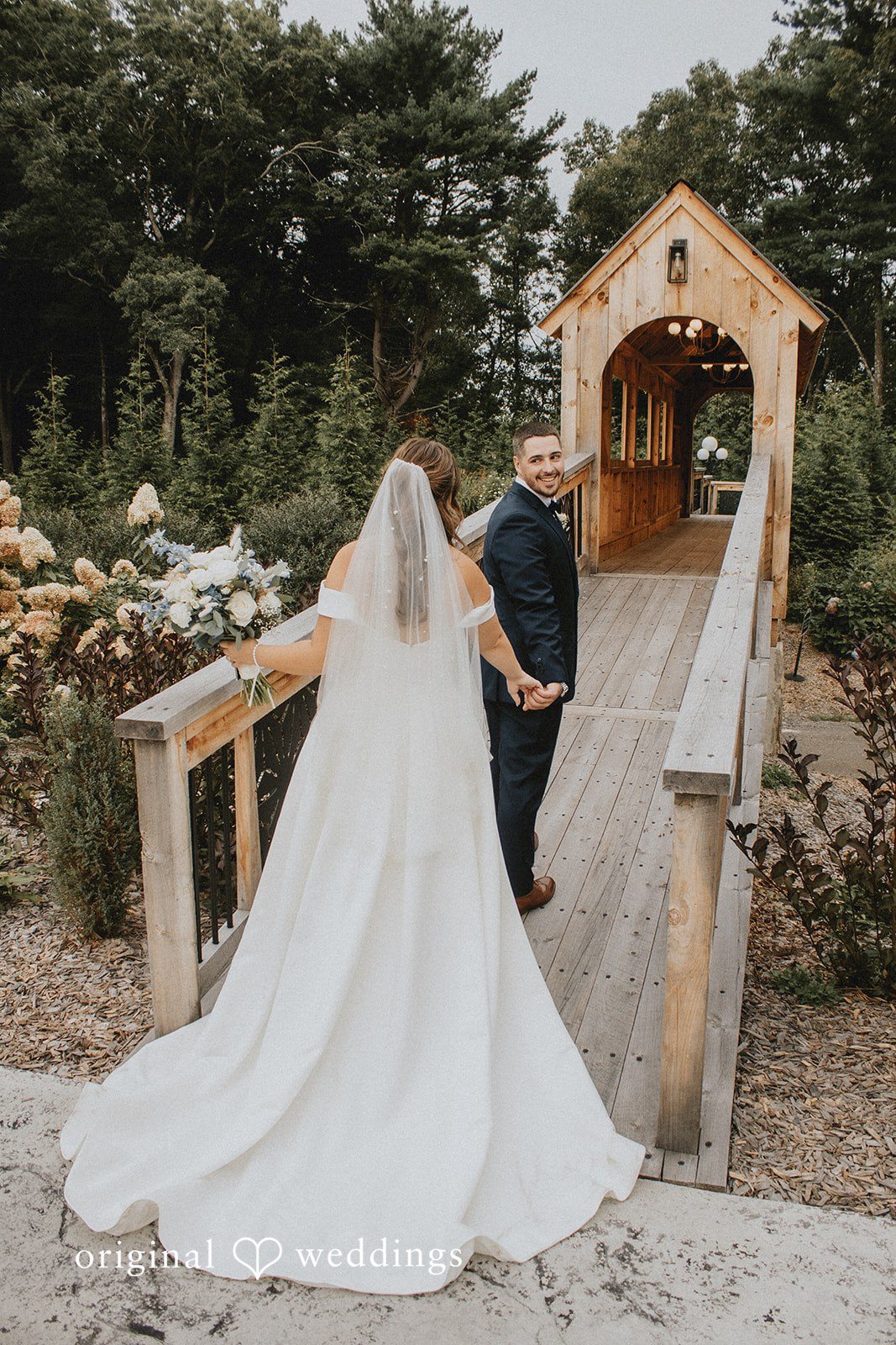 Sarah + Christopher A bride and groom standing on a small wooden bridge surrounded by trees.