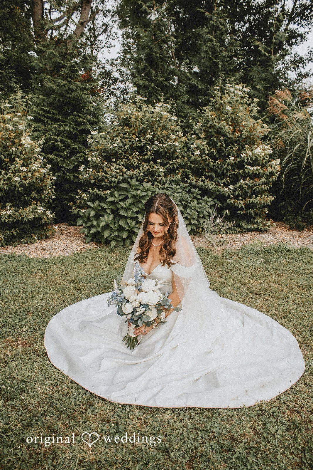 September 19, 2026 – Sarah & Christopher – (ID-4569) A bride in a white gown sitting down in a grassy field.