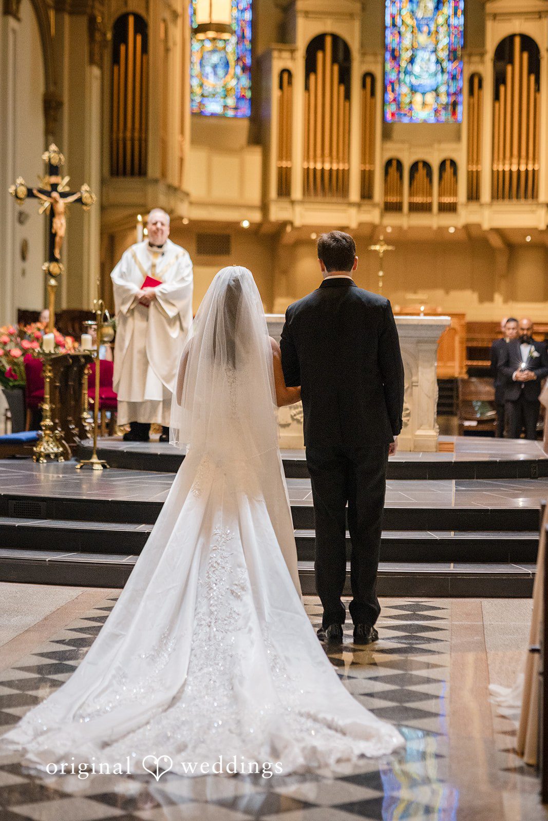 John + Michelle Bride in a long wedding gown walking down a church aisle.