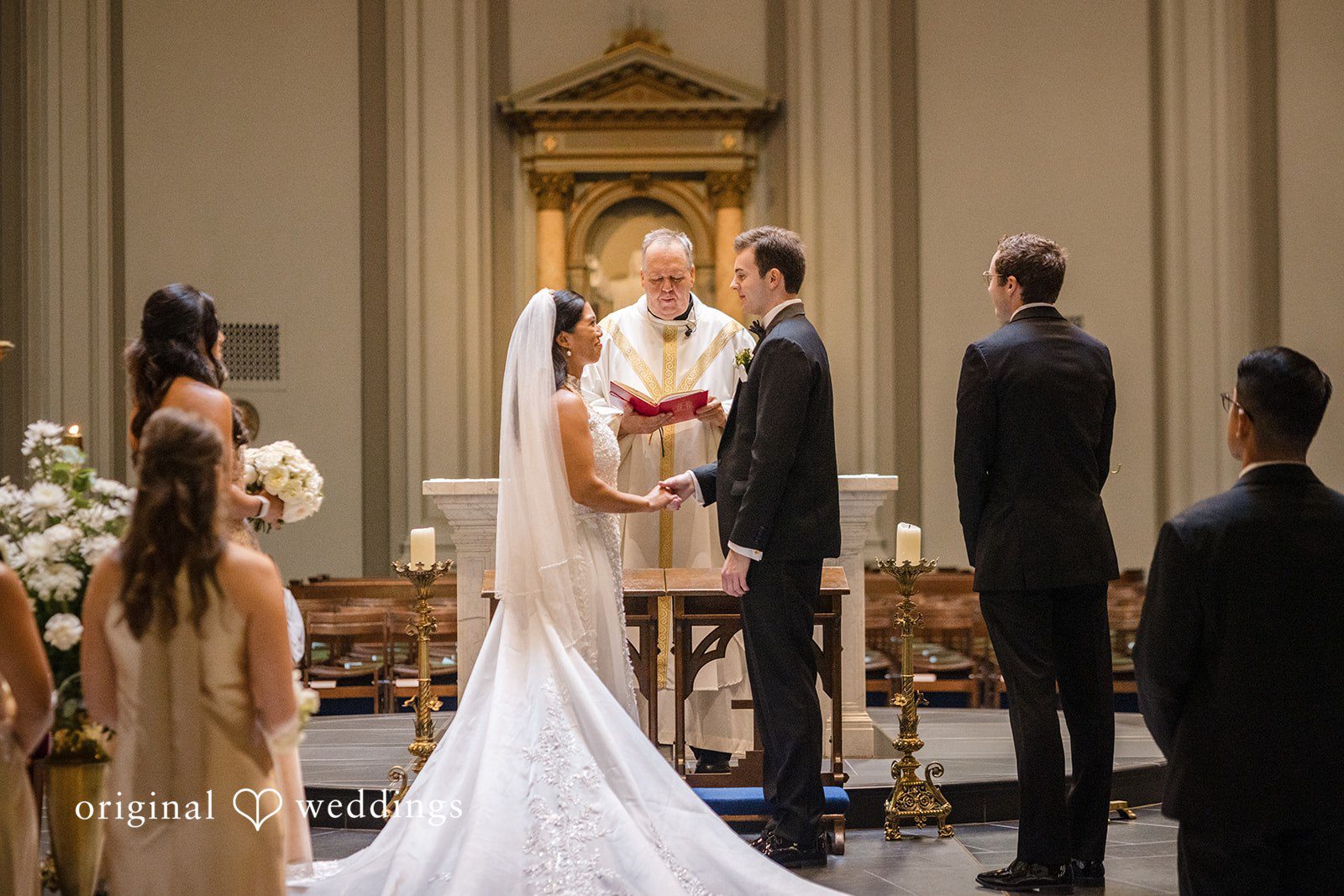 John + Michelle Bride and groom standing before a priest at a church altar.