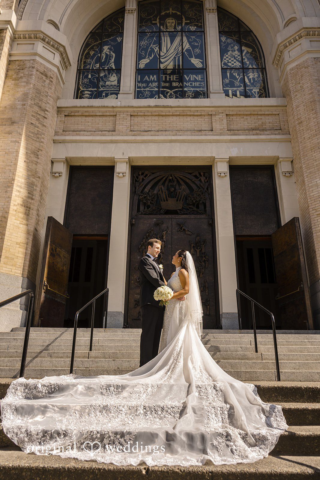 John + Michelle Bride and groom standing on a grand exterior steps with a long veil trailing behind.