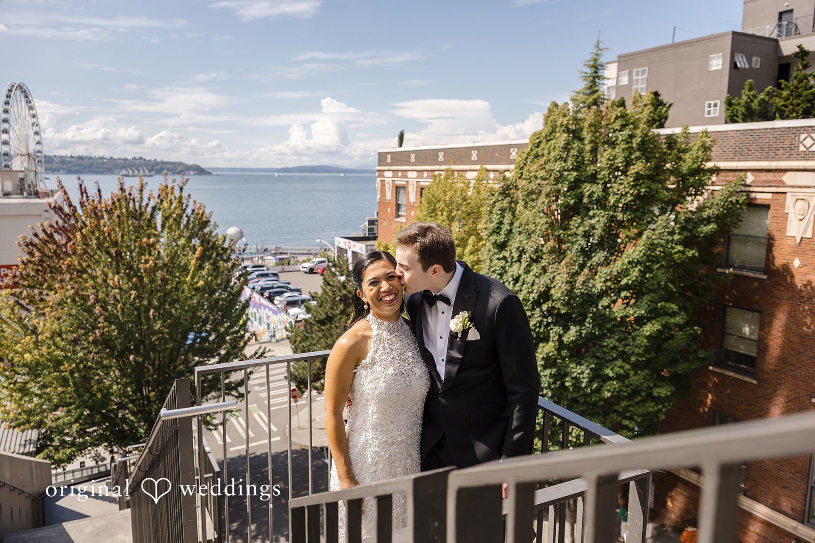 John + Michelle Bride and groom posing on an elevated walkway surrounded by greenery.