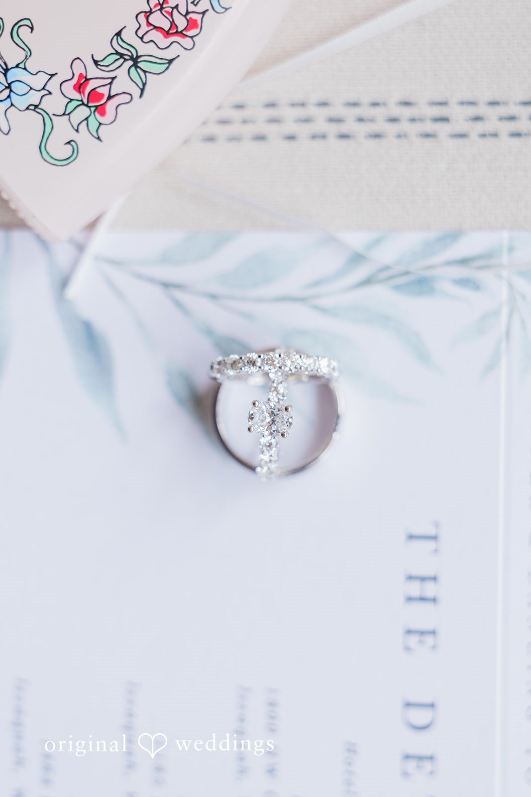 Kim + Keven A close-up of a wedding invitation card and rings.