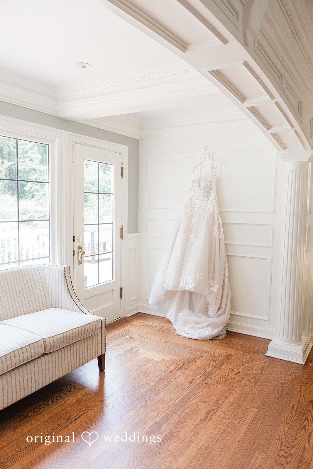 Kim + Keven A room with a wooden floor and a wedding dress hanging in the background.