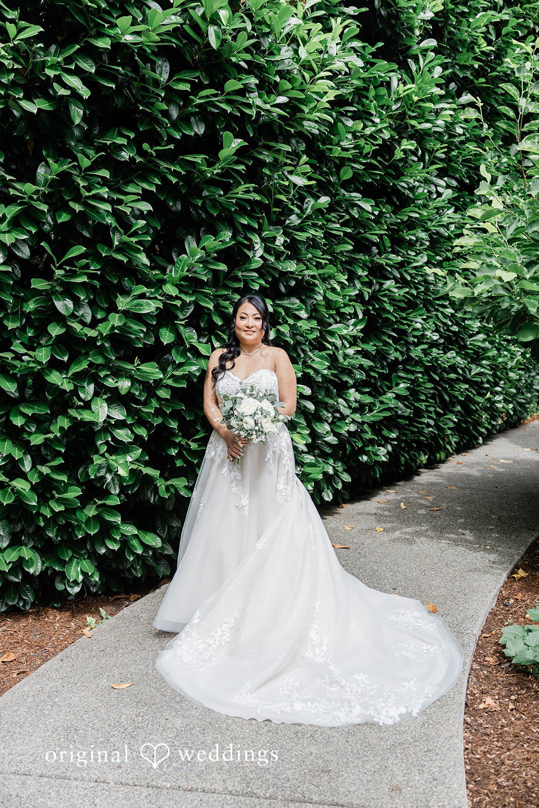 Kim + Keven A bride in a white gown posing against a hedge.