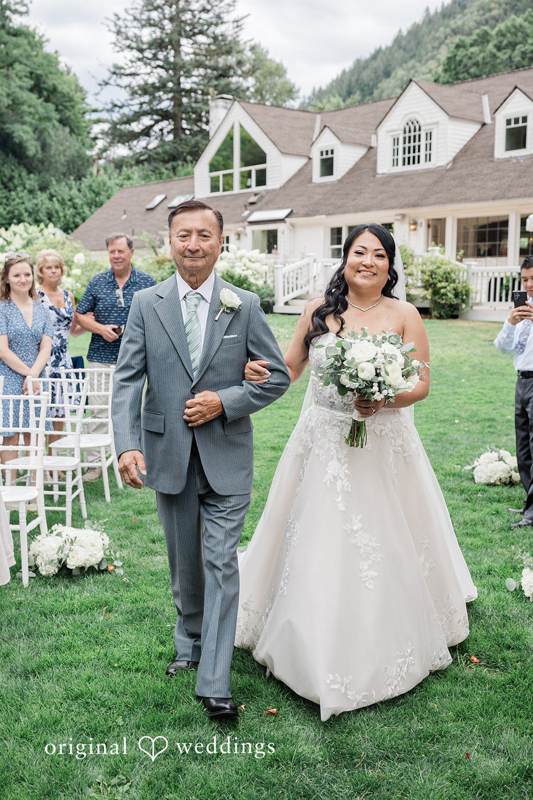 Kim + Keven A bride and man walking across a lawn toward an estate.