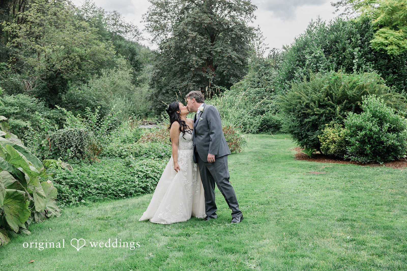 Kim + Keven A bride and groom embracing on a grassy field surrounded by trees.