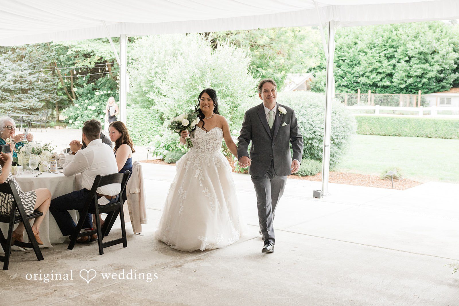 Kim + Keven A bride and groom walking together under a white tent structure.