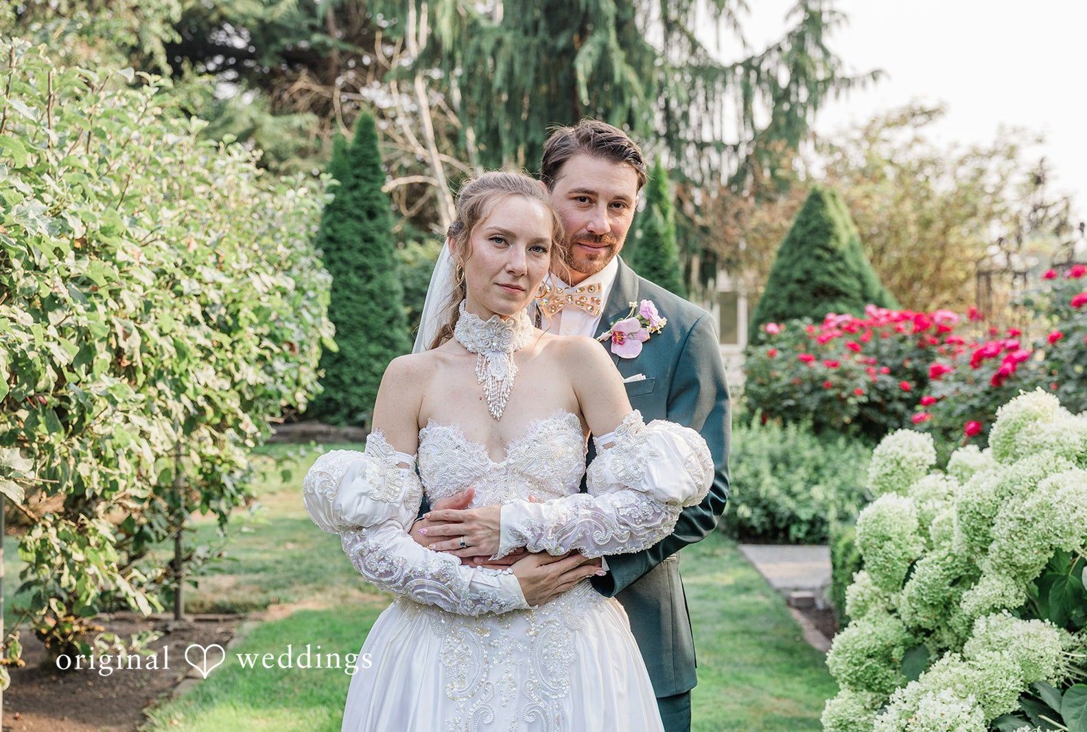 Bride and groom embracing among white hydrangeas and red roses, captured by Seattle wedding photographers from Original Weddings at Genesis Farm and Gardens