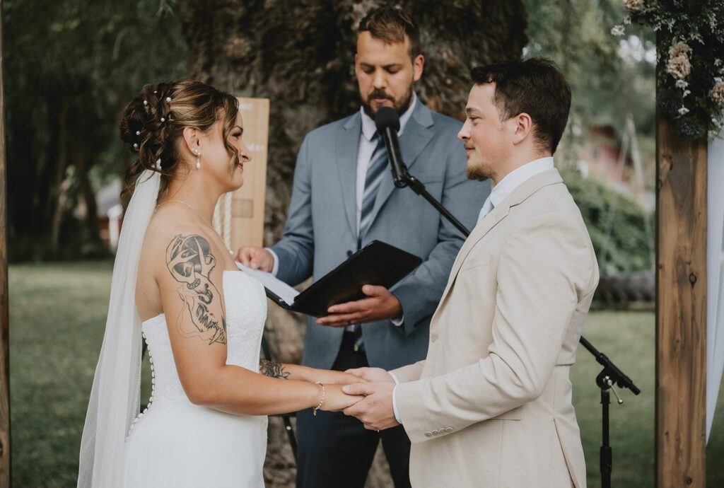 Good Tree Farmstead Wedding | Madelyn & David 5 Madelyn and David holding hands during their outdoor ceremony, captured by Minneapolis wedding photographers from Original Weddings at Good Tree Farmstead