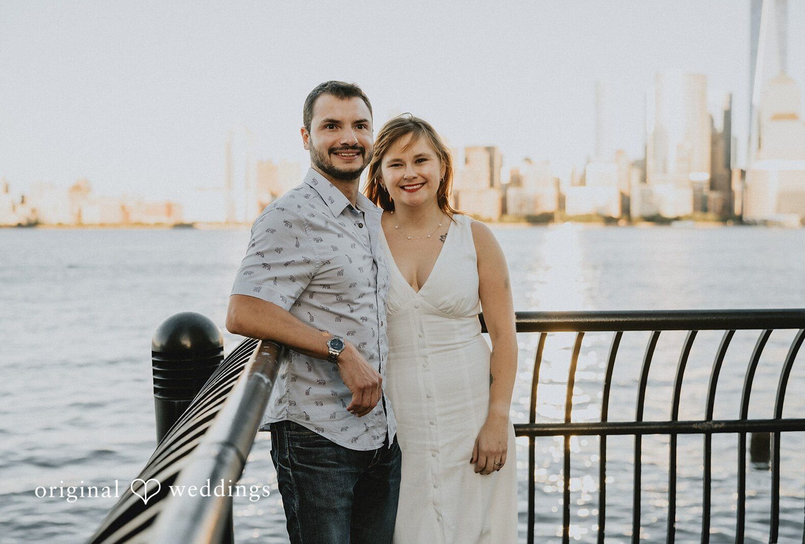 Scottie and Richie smiling by the river with the Manhattan skyline behind them, captured by Engagement Photography Services from Original Weddings at Grace O'Malley's
