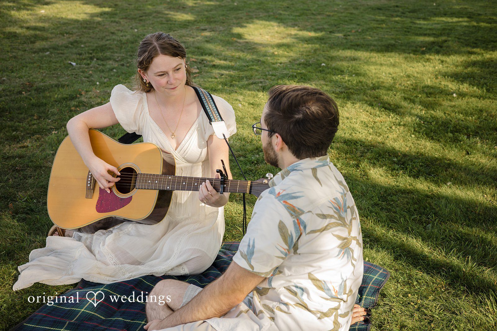 James + Ashlan A woman sits playing a guitar while a man sits nearby facing her.