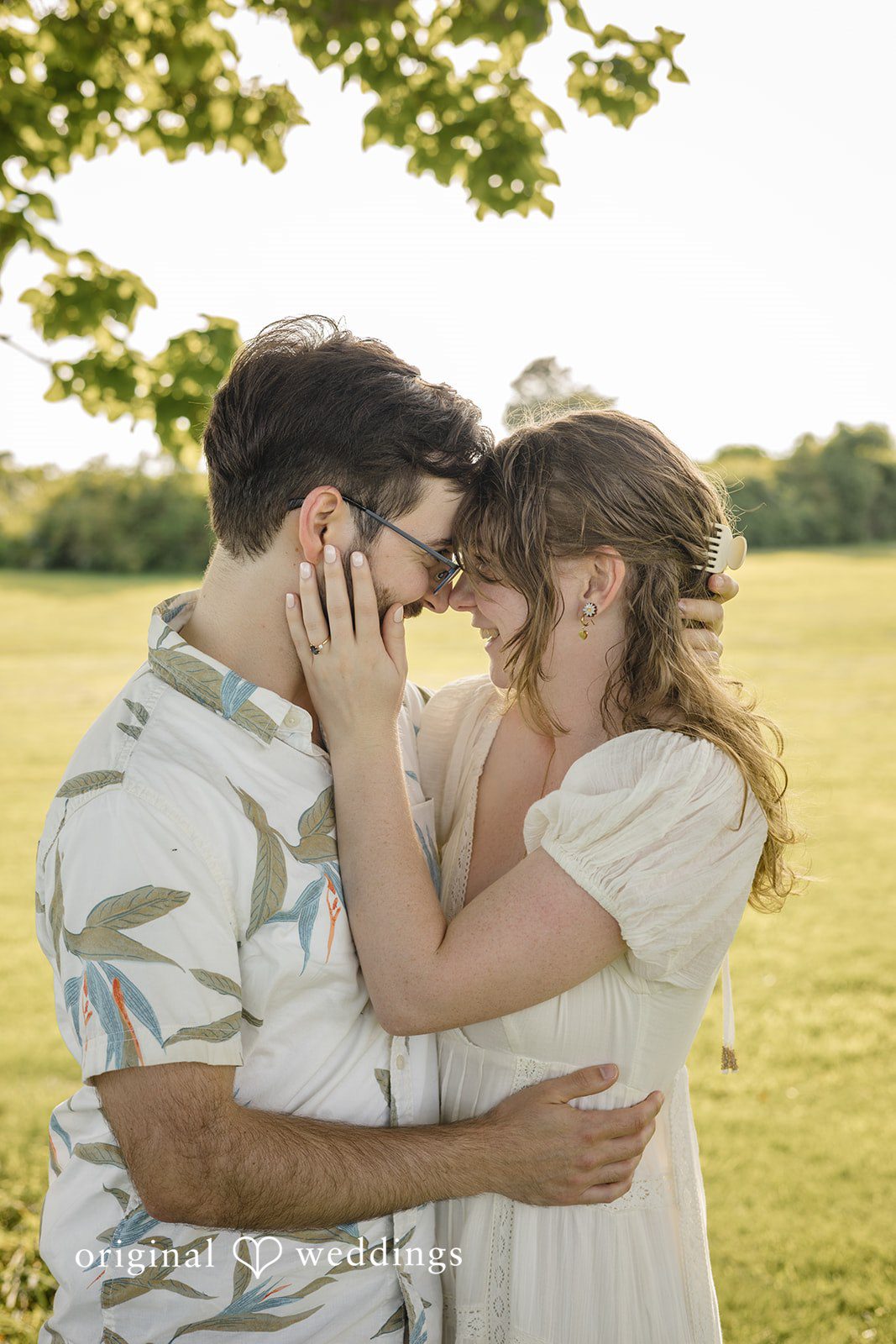 James + Ashlan A man and a woman embrace closely while standing in a grassy field.