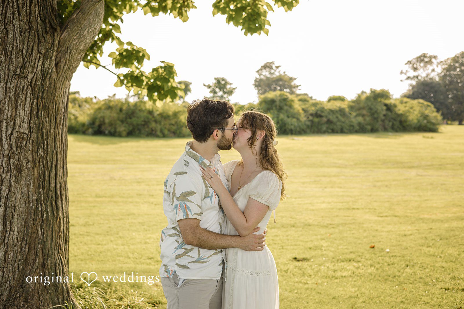 James + Ashlan A man and a woman share a close embrace standing under a large tree.