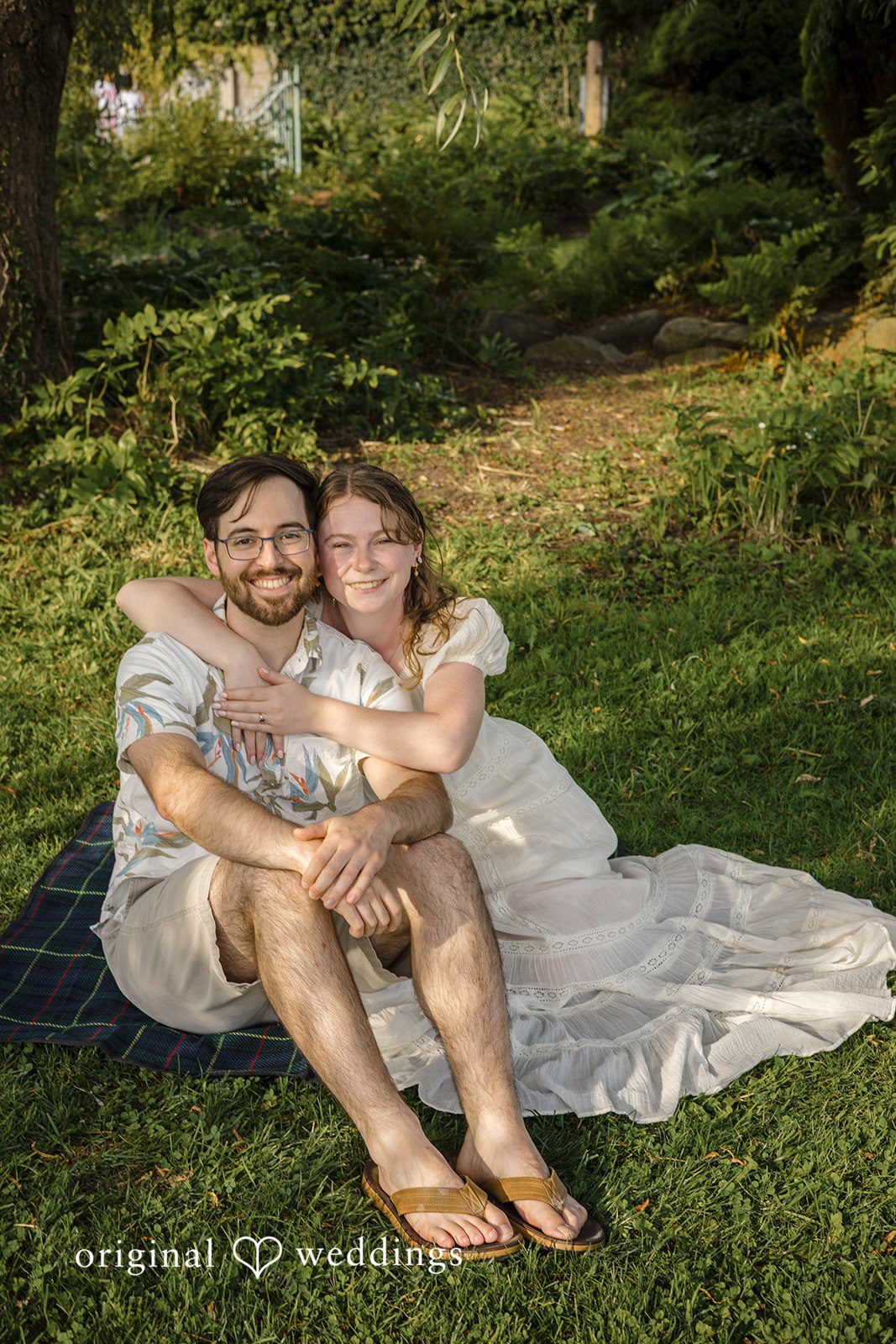 James + Ashlan A man sits on a grassy hill holding a woman on his lap.