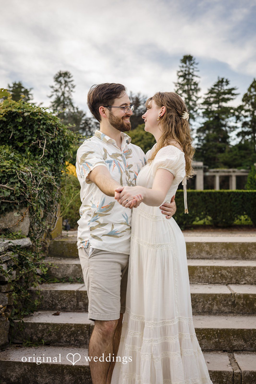 James + Ashlan A man and a woman hold hands while standing on stone steps next to a balustrade.