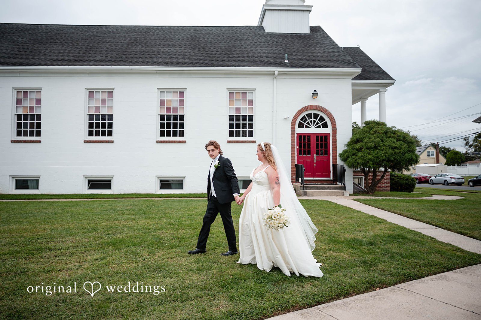 Bethany + Eddie Couple walking across the church lawn, captured by Philadelphia wedding photographers from Original Weddings