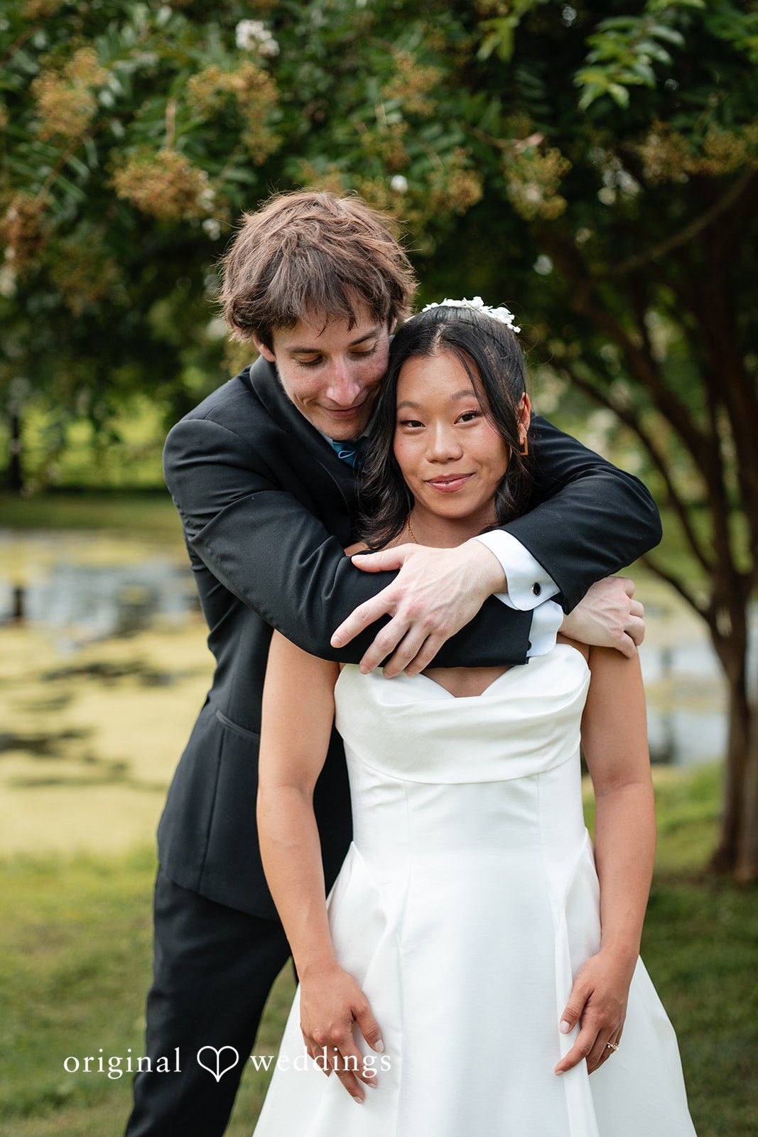 Mae + Corey A groom embraces a bride from behind while posing together.