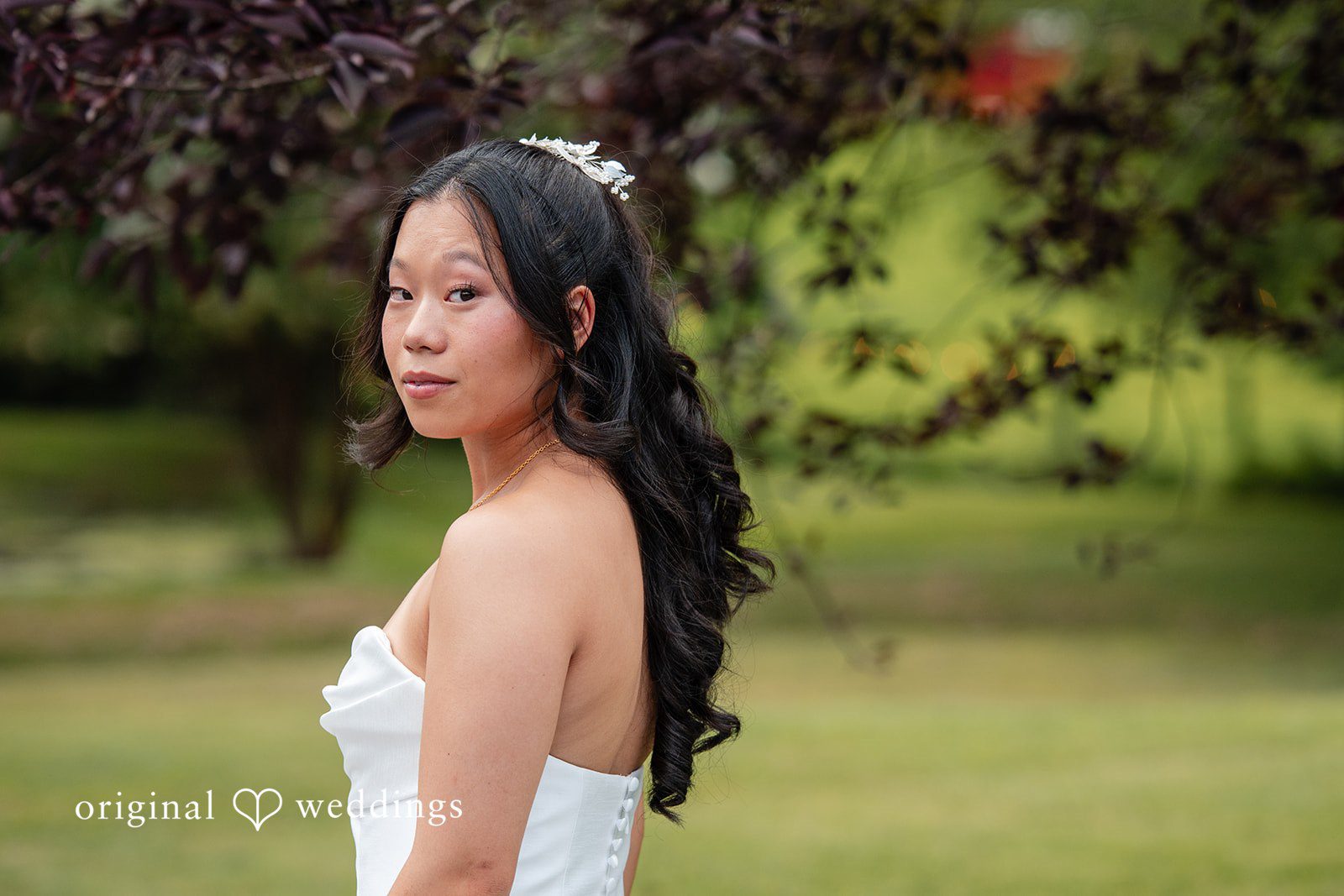 Mae + Corey A bride with long dark hair poses looking over her shoulder against a green background.