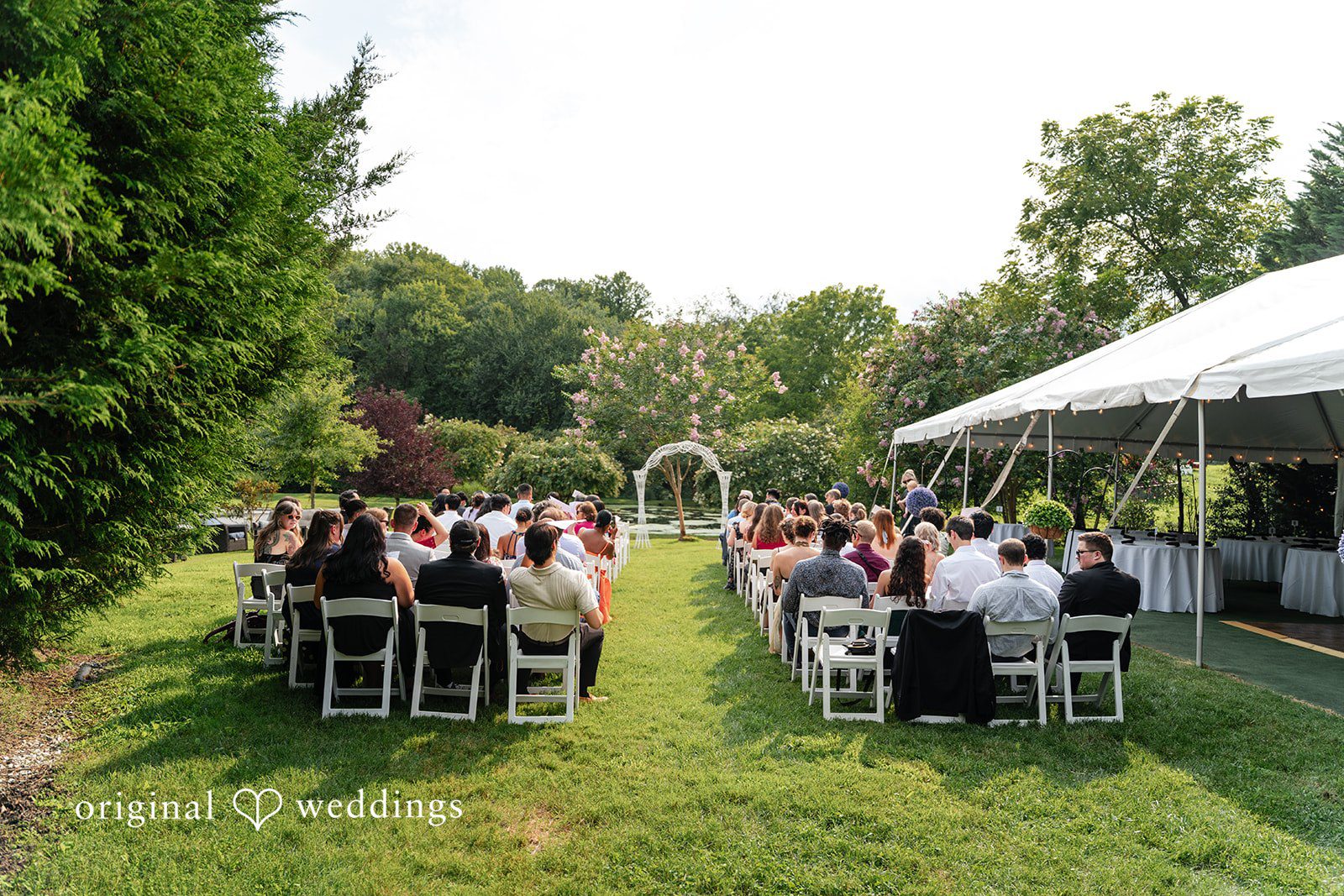 Mae + Corey An elevated view of guests seated for a wedding ceremony in a large green yard.