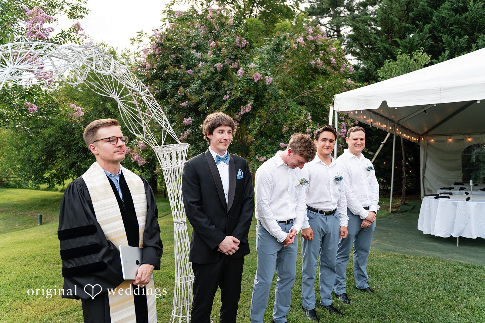 Mae + Corey An officiant and groomsmen stand ready near a white tent before a wedding ceremony.