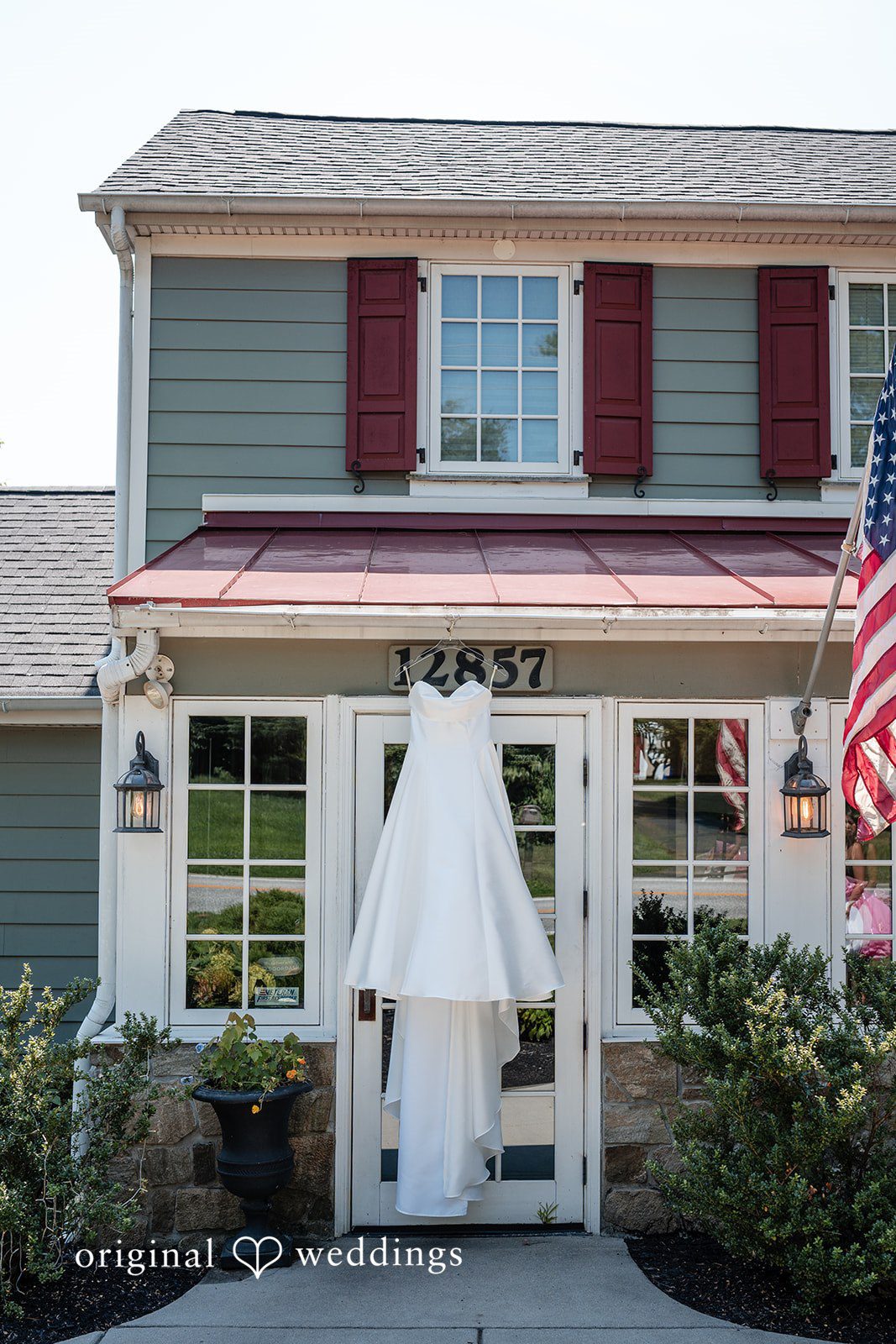 Mae + Corey A white wedding dress hangs on the front porch of a two-story residential house.