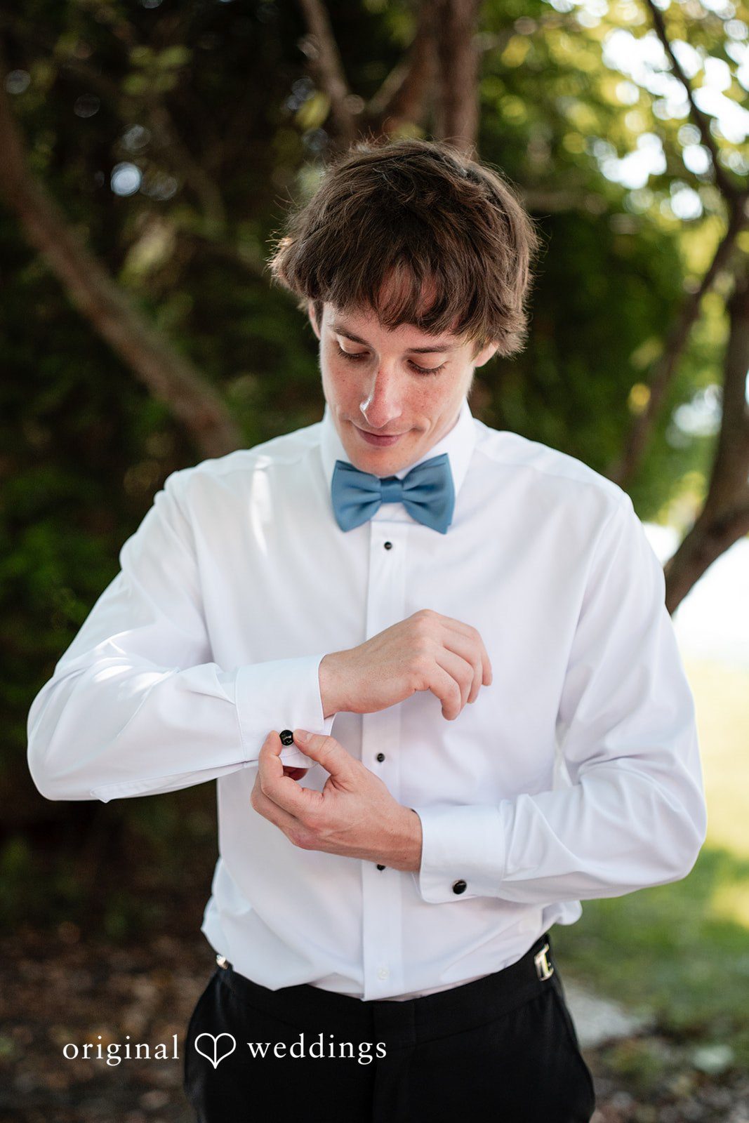 Mae + Corey Groom adjusts his teal bowtie while getting dressed in a white button-down shirt.