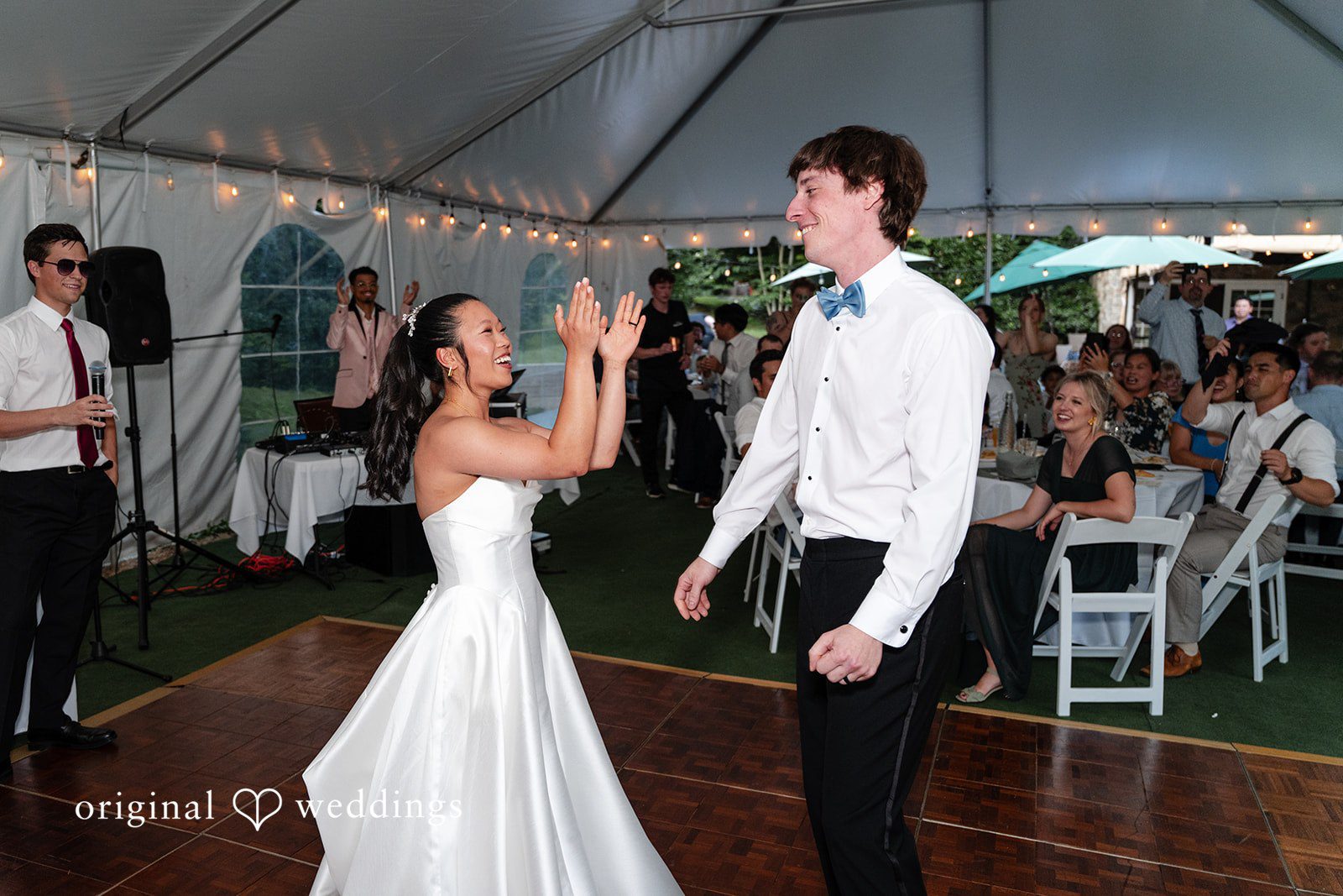 Mae + Corey • A bride and groom celebrate playfully with their arms raised on a wooden dance floor inside a tent.