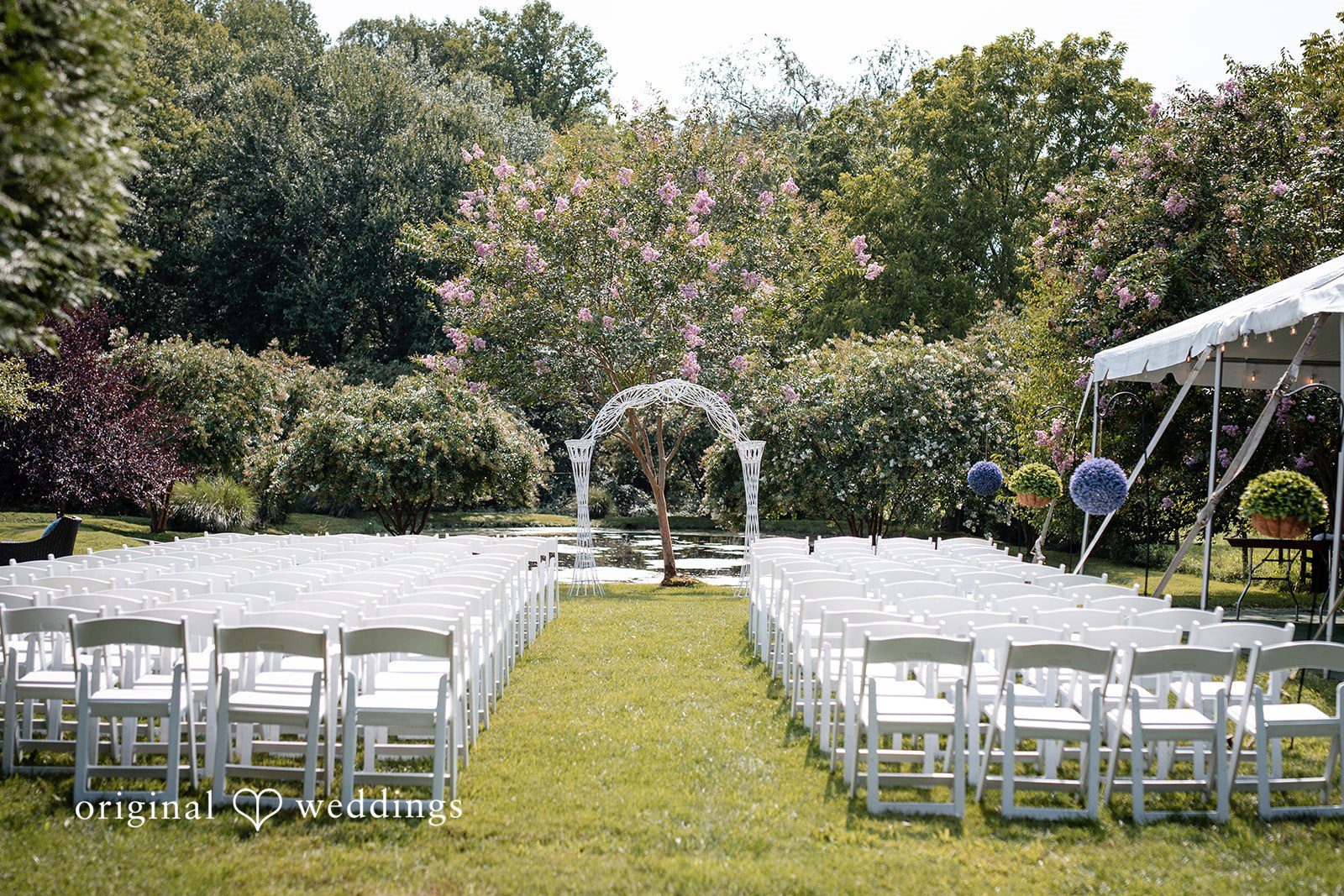 Mae + Corey An empty wedding ceremony setup with white chairs facing an altar in a garden.
