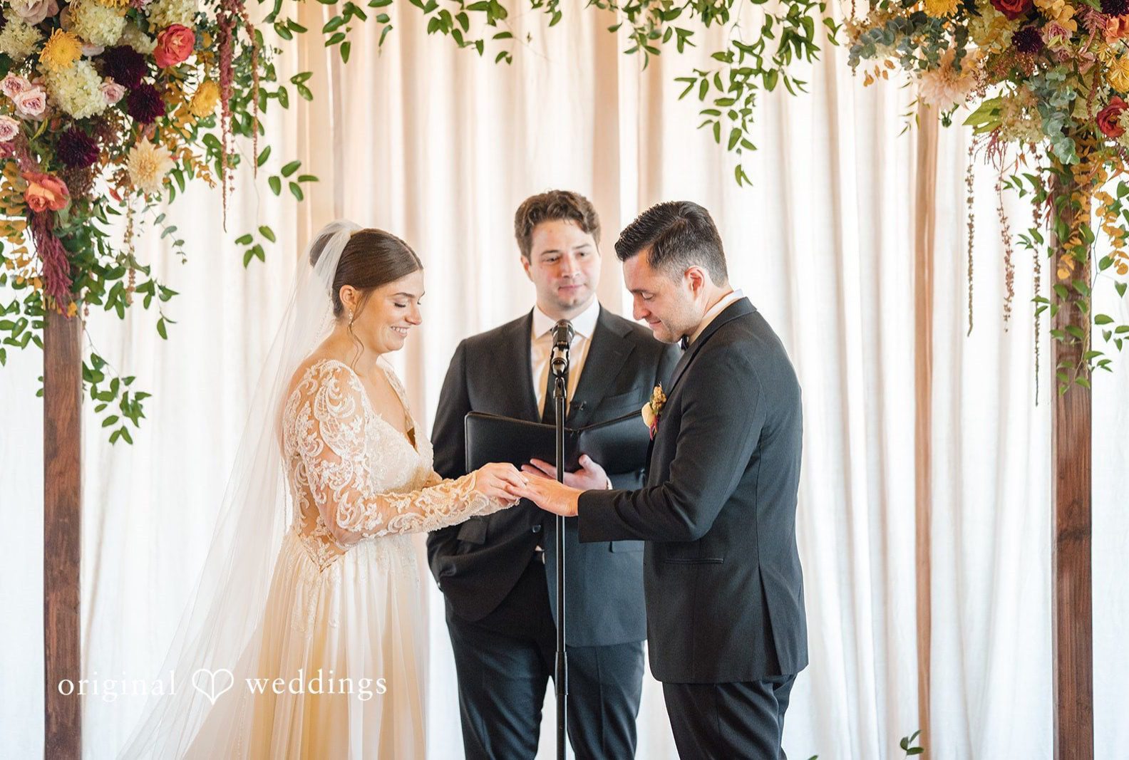 Bride and groom exchanging rings under the floral arch, captured by Chicago wedding photographers from Original Weddings at Lacuna Lofts