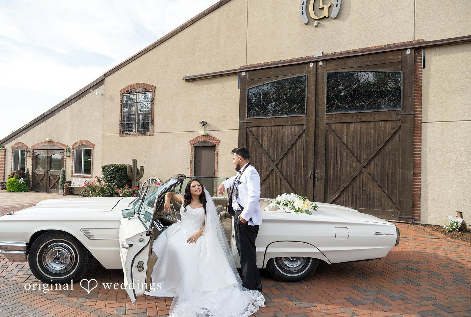 Bride and groom with a vintage white car and barn doors behind them, captured by Chicago wedding photographers from Original Weddings at Rancho Los Guzman