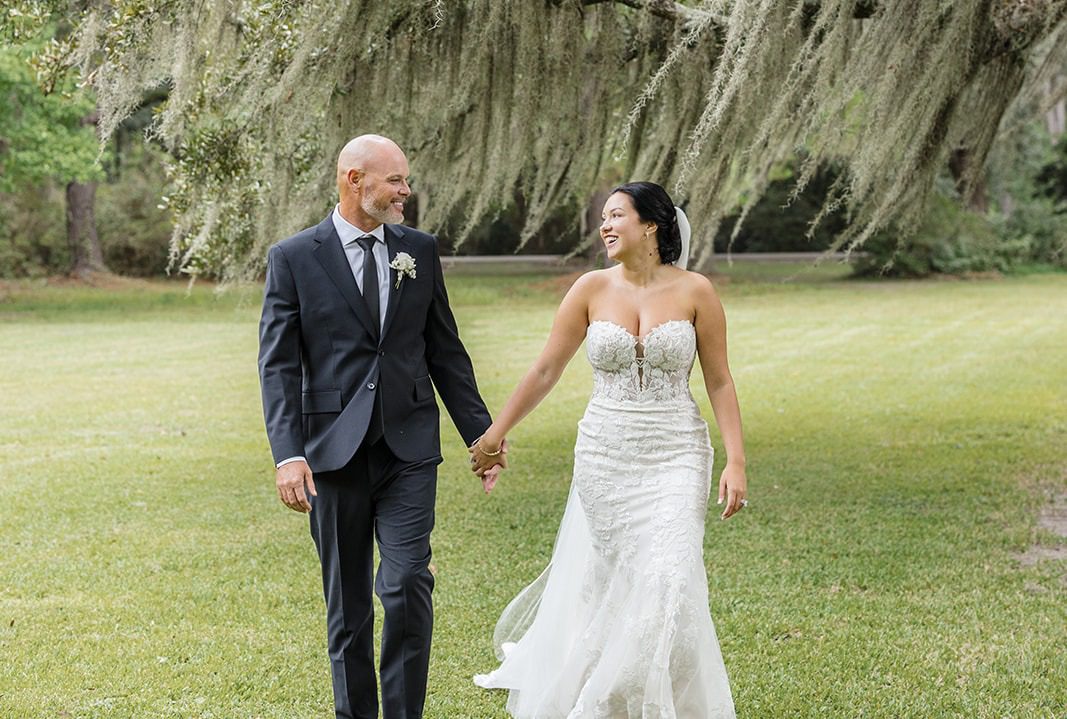 Haily and Mackie walking hand in hand on the lawn under the live oaks, captured by Charleston wedding photographers from Original Weddings at Magnolia Plantation and Gardens