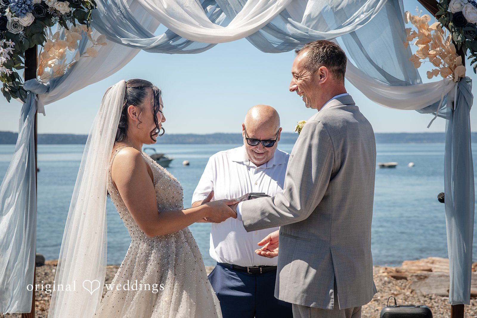 Kelly + John Couple exchanging rings by the water, captured by Seattle wedding photographers from Original Weddings at Mckees Beach