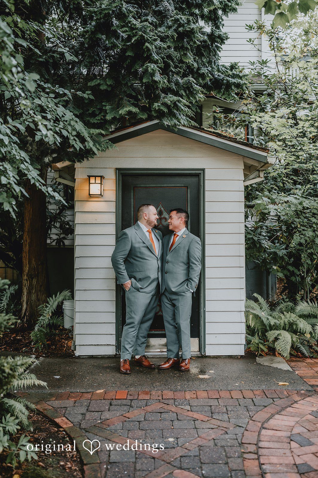 Benjamin + Tuan Grooms standing together by a small garden shed