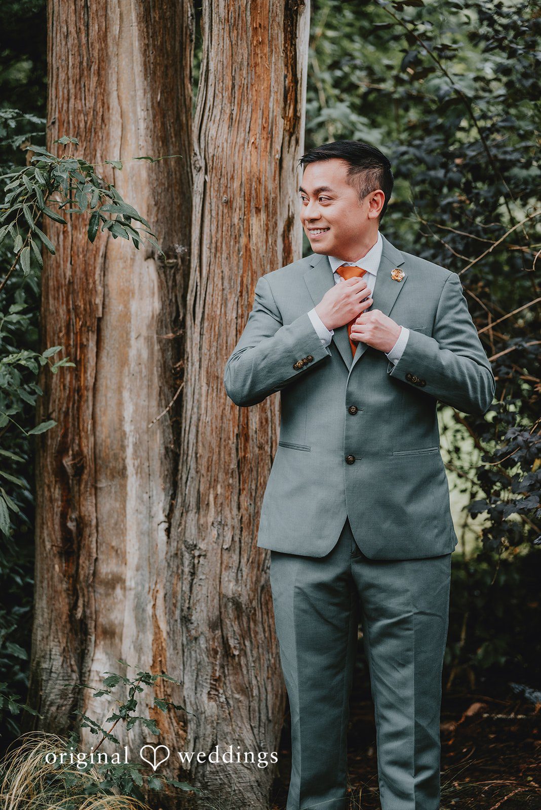 Benjamin + Tuan Groom in a gray suit posing by a large tree