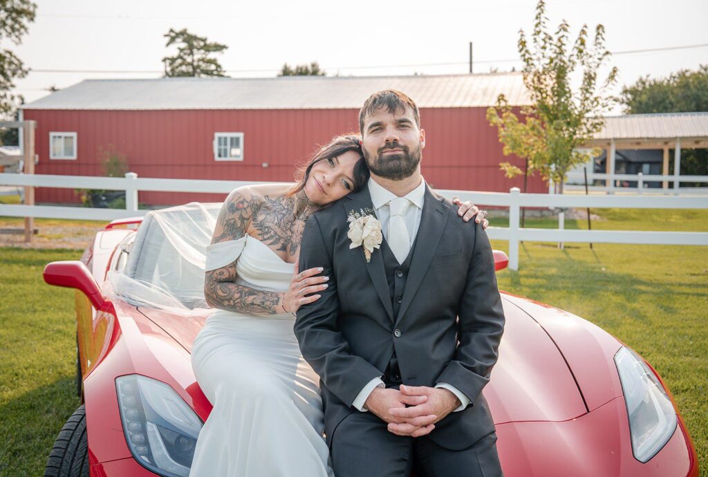 Minneapolis Wedding Photographers at The Midway | Sarah & Drew 13 Bride and groom smiling by the red car with the barn behind them, captured by Minneapolis wedding photographers from Original Weddings at The Midway