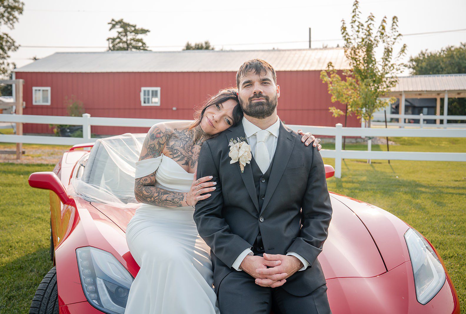 Bride and groom smiling by the red car with the barn behind them, captured by Minneapolis wedding photographers from Original Weddings at The Midway
